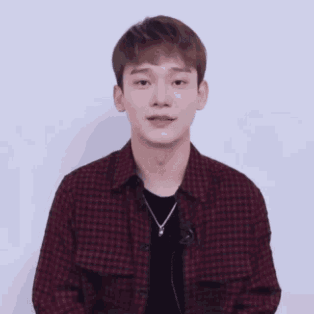 a man wearing a plaid shirt and a necklace is laughing with his eyes closed