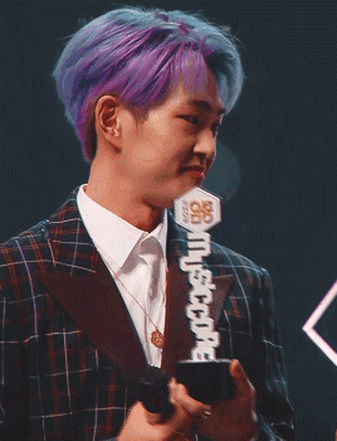 a man with purple hair is holding a microphone and a trophy that says ' nct ' on it