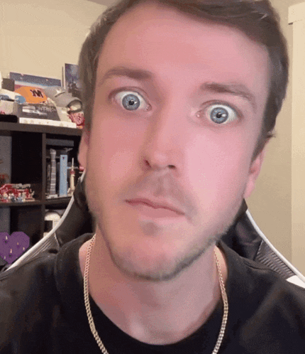 a man wearing a black shirt and a gold chain is making a surprised face