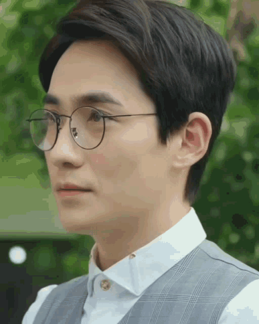a man wearing glasses and a vest looks to the side