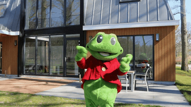 a green frog mascot in front of a large house