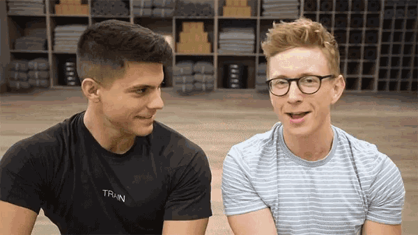 a man wearing glasses and a black shirt that says train talks to another man