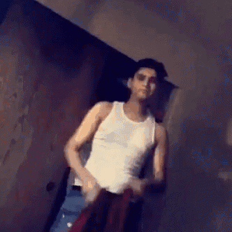 a man in a white tank top is standing in front of a wall .