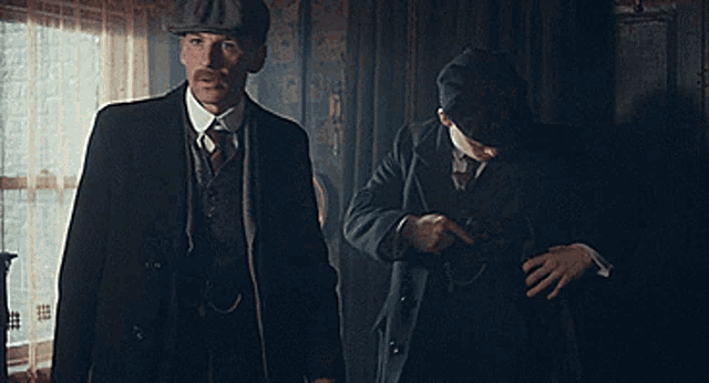 two men in suits and hats are standing in a room