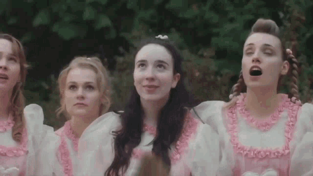 a group of women in pink and white dresses are singing and looking up