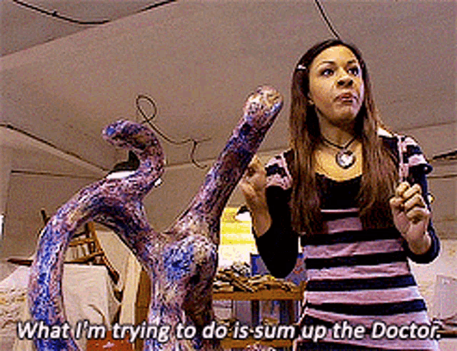 a woman is standing in front of a sculpture and says " what i 'm trying to do is sum up the doctor "