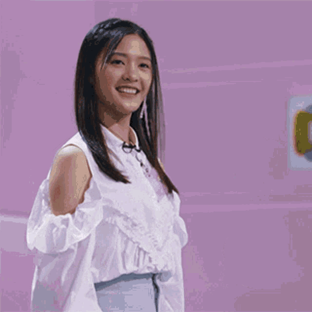 a woman in a white shirt stands in front of a purple wall with ok written in yellow letters