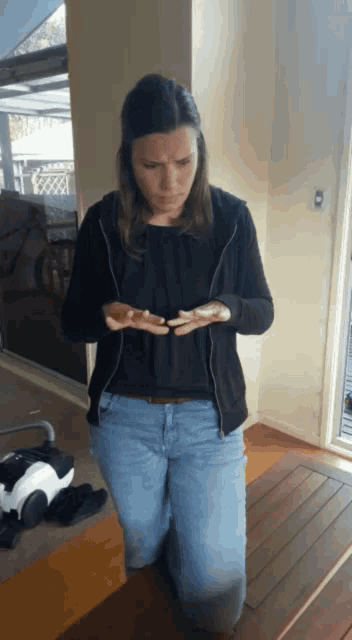 a woman in a black jacket and blue jeans is kneeling on the floor