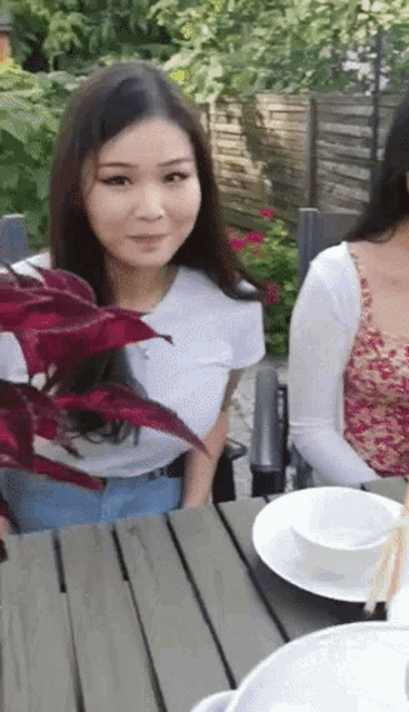 a woman in a white shirt is sitting at a table with a bowl on it