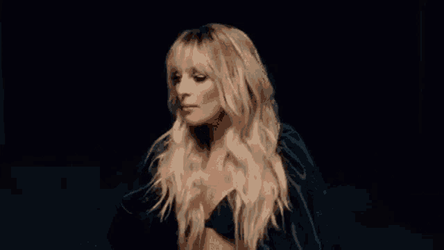 a woman with long blonde hair and bangs is wearing a black top and a black jacket .
