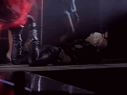 a person laying on their stomach on a stage with their feet up and a person in a red dress in the background