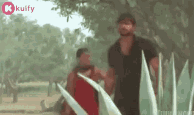 two men are standing next to each other in a park holding hands .