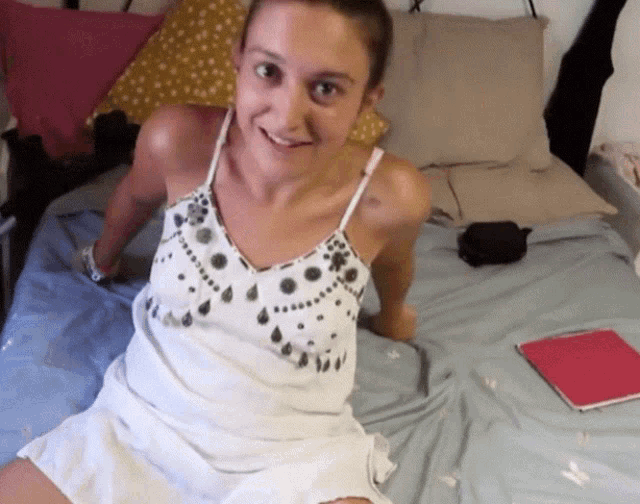 a woman in a white dress sits on a bed smiling