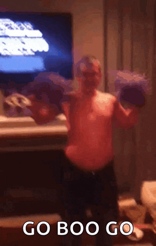 a man without a shirt is lifting a dumbbell in front of a television and says `` go boo go '' .