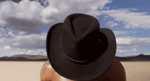 a man wearing a black fedora hat stands in the desert