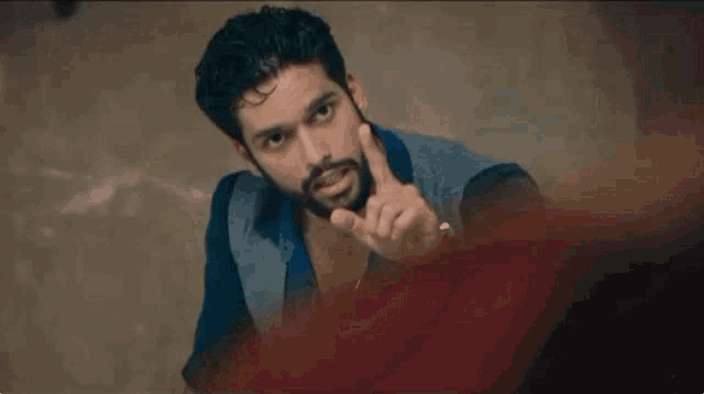 a man with a beard is pointing his finger at the camera while wearing a watch .
