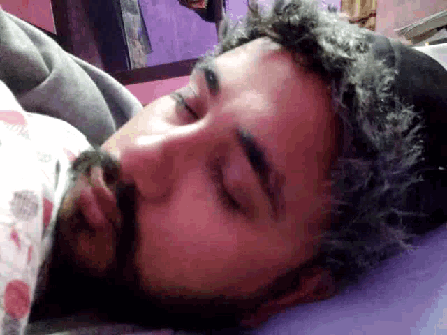 a man with a beard is sleeping in a bed with his eyes closed
