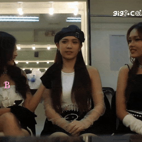 three women are sitting in front of a mirror with a pink b on the bottom