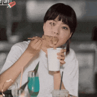 a woman is eating a piece of food and drinking from a paper cup