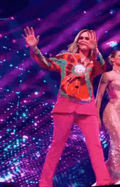 a woman in a pink suit is waving at the camera