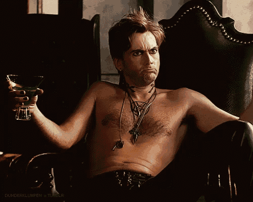 a shirtless man sits in a chair holding a martini