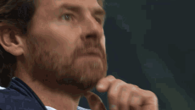 a man with a beard wearing a blue jacket looks to the side