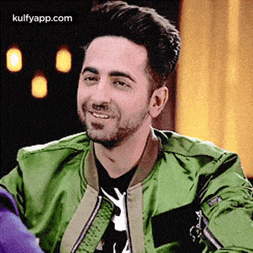 a man wearing a green jacket is smiling and looking at the camera .