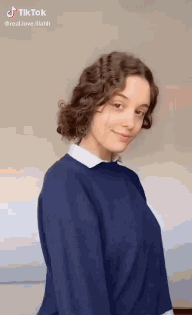 a girl with curly hair is wearing a blue sweater and white shirt .