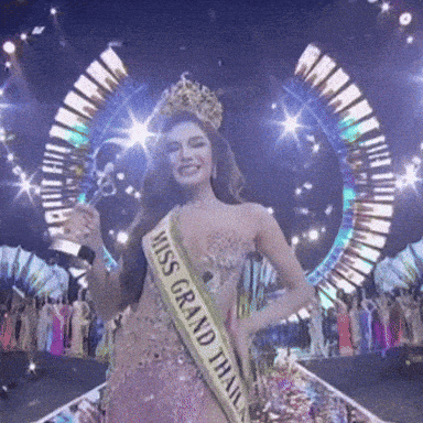 a woman wearing a miss grand thailand sash holds a trophy