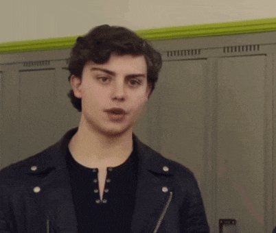 a young man wearing a black leather jacket and a black shirt is standing in front of lockers .