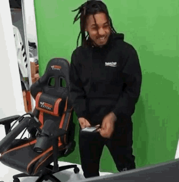 a man with dreadlocks is standing in front of a green screen and holding a cell phone .