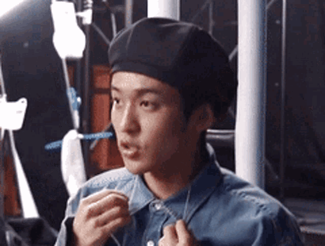 a man wearing a beret and a denim shirt is adjusting his tie