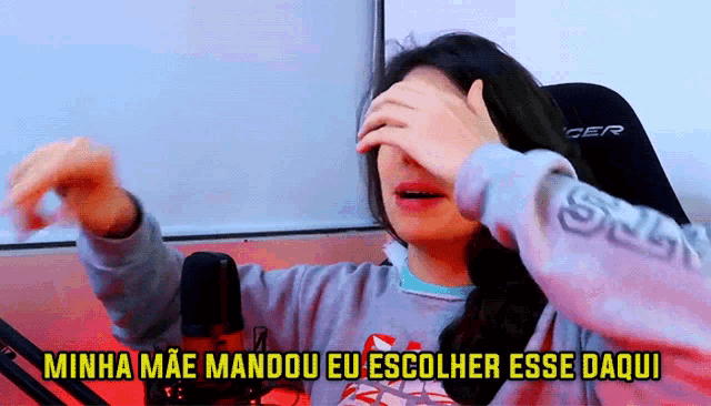 a woman covering her face in front of a microphone with the words " minha mae mandou eu escolher esse daqui " below her