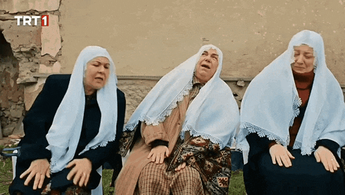 three women wearing shawls sit in front of a wall that says trt1