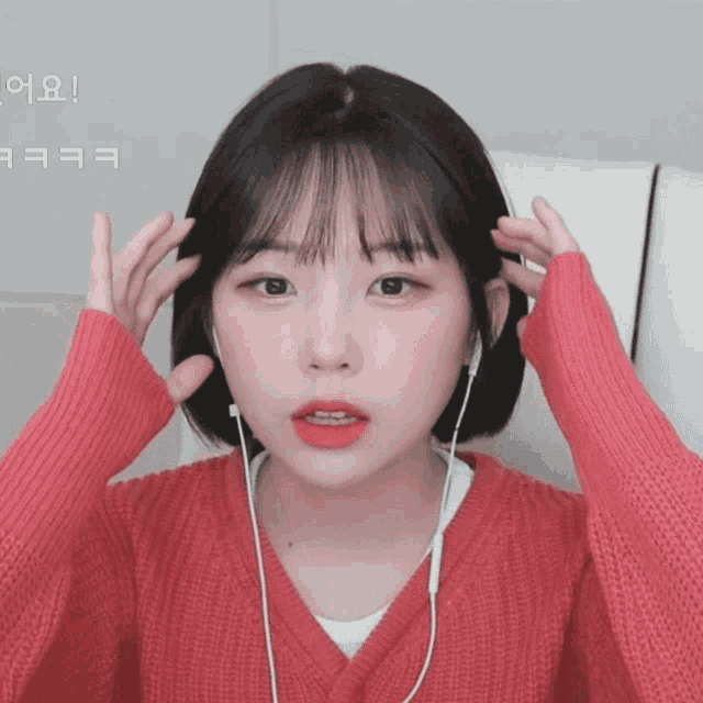 a girl wearing a red sweater and ear buds holds her hair