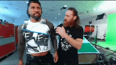 two men are standing next to each other in a room with a green screen behind them .