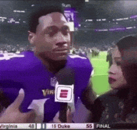 a man in a purple vikings jersey is talking to a woman with a microphone .