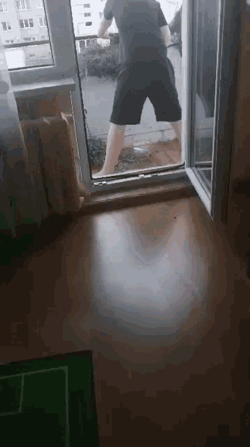 a man in black shorts is standing on a balcony looking out a window .