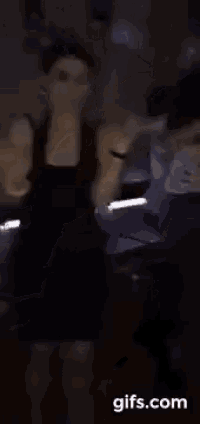 a woman is dancing in a dark room while wearing a black tank top .