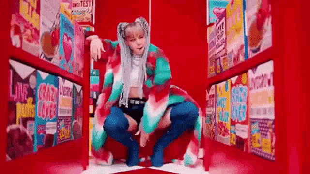 a woman in a colorful outfit is kneeling down in front of a red wall filled with boxes of cereal .