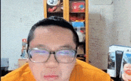 a man wearing glasses and a yellow shirt is making a funny face in a room .