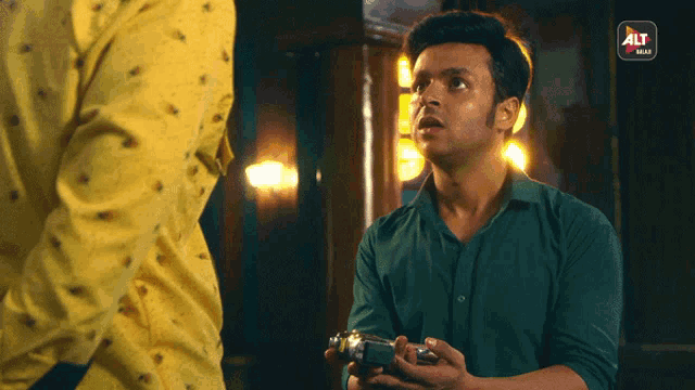 a man in a green shirt is holding a camera in front of a man in a yellow shirt that says alt