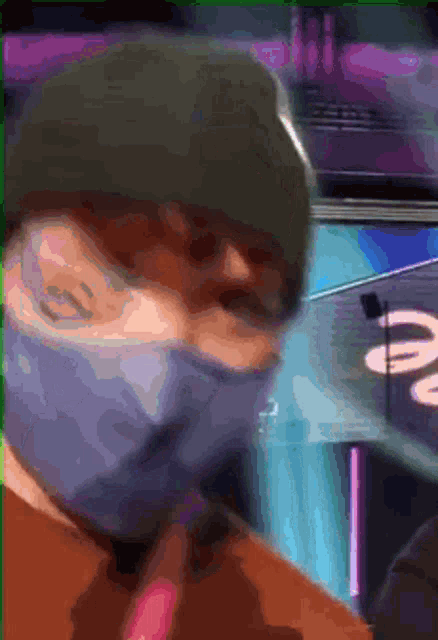 a man wearing a mask and a beanie is standing in front of a sign that says ' a ' on it