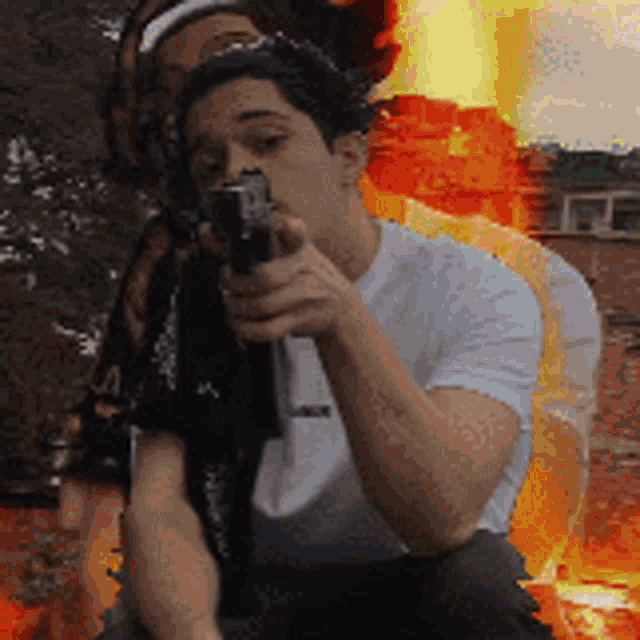 a man in a white shirt is holding a gun in front of a fire background