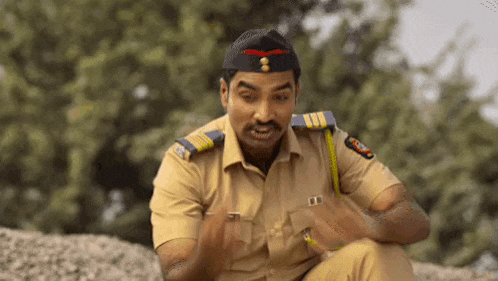 a man in a police uniform is sitting on a pile of gravel and making a funny face .