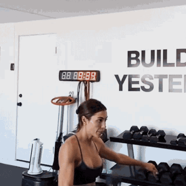a woman in a gym with a sign on the wall that says build yesterd