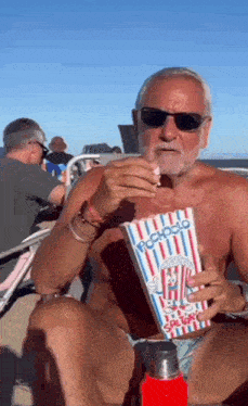 a man without a shirt is eating popcorn from a bag that says popcorn