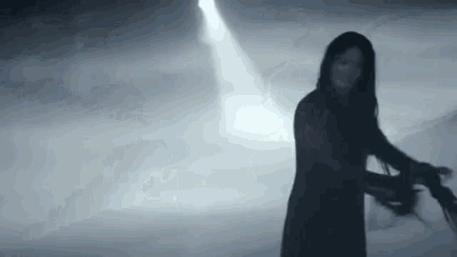 a woman in a black dress is standing in a dark room holding a sword .