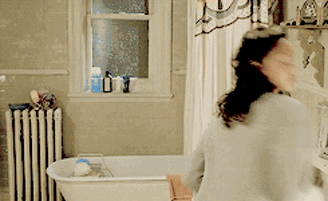a woman is brushing her hair in a bathroom next to a tub