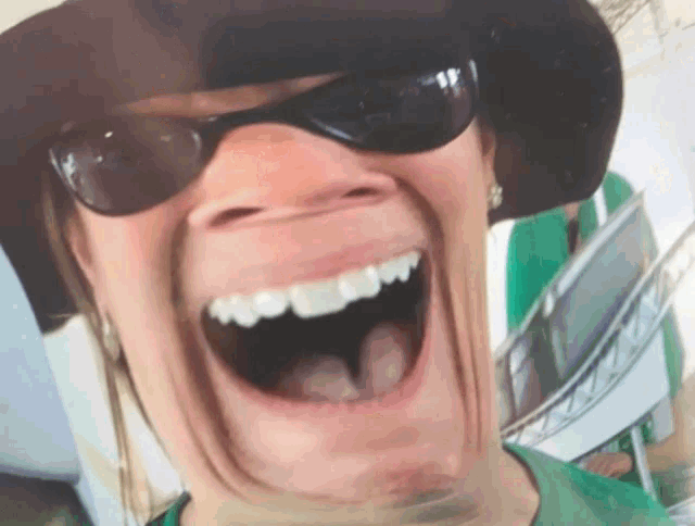 a woman wearing sunglasses and a hat is smiling with her mouth wide open